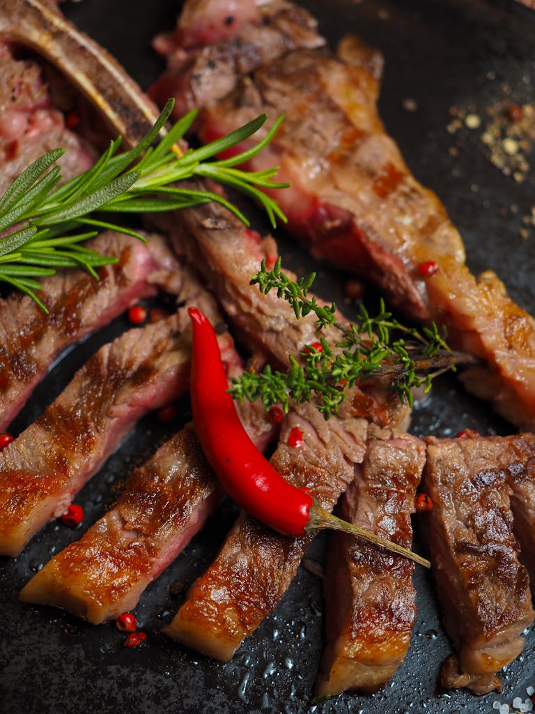 Close-up of a sliced grilled steak garnished with herbs and chili pepper.
